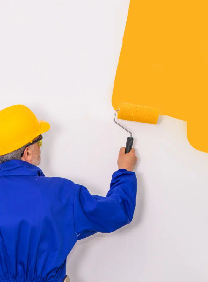 Peintre en bleu de travail avec rouleau sur peinture jaune